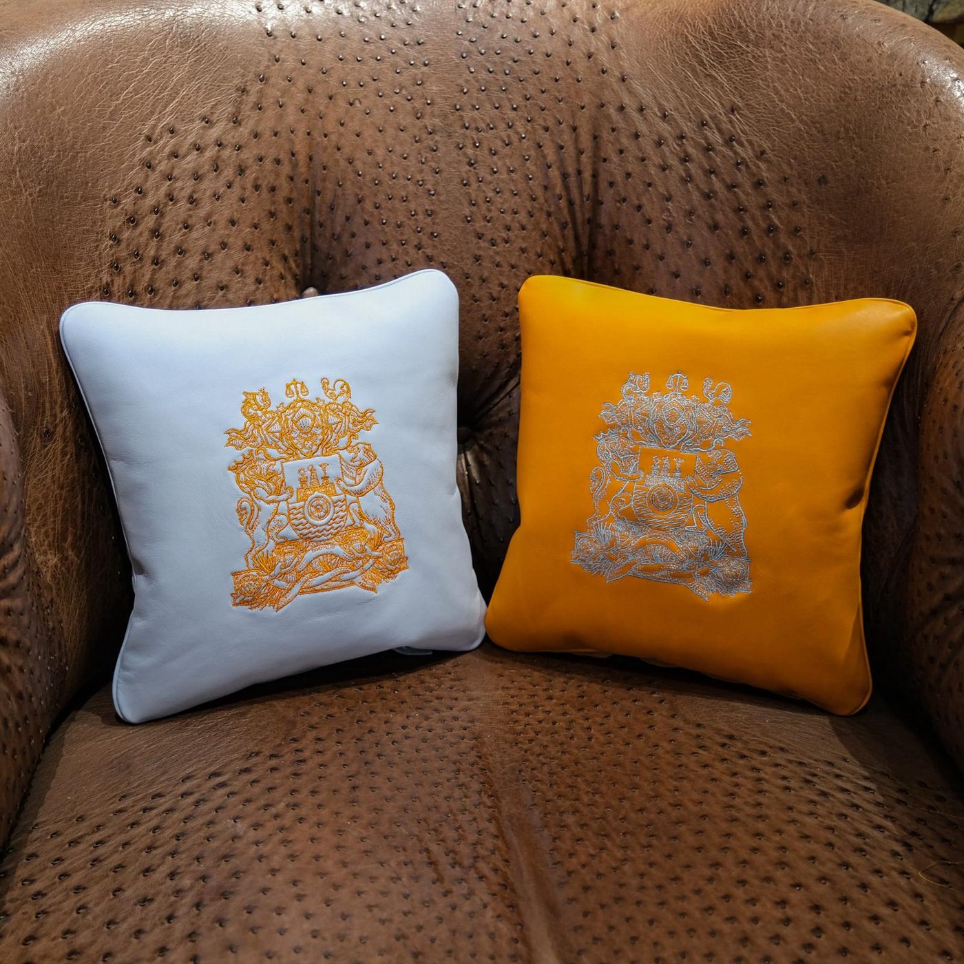 Deux coussins en cuir, bleu ciel et orange, brodés d'un blason sur un fauteuil club