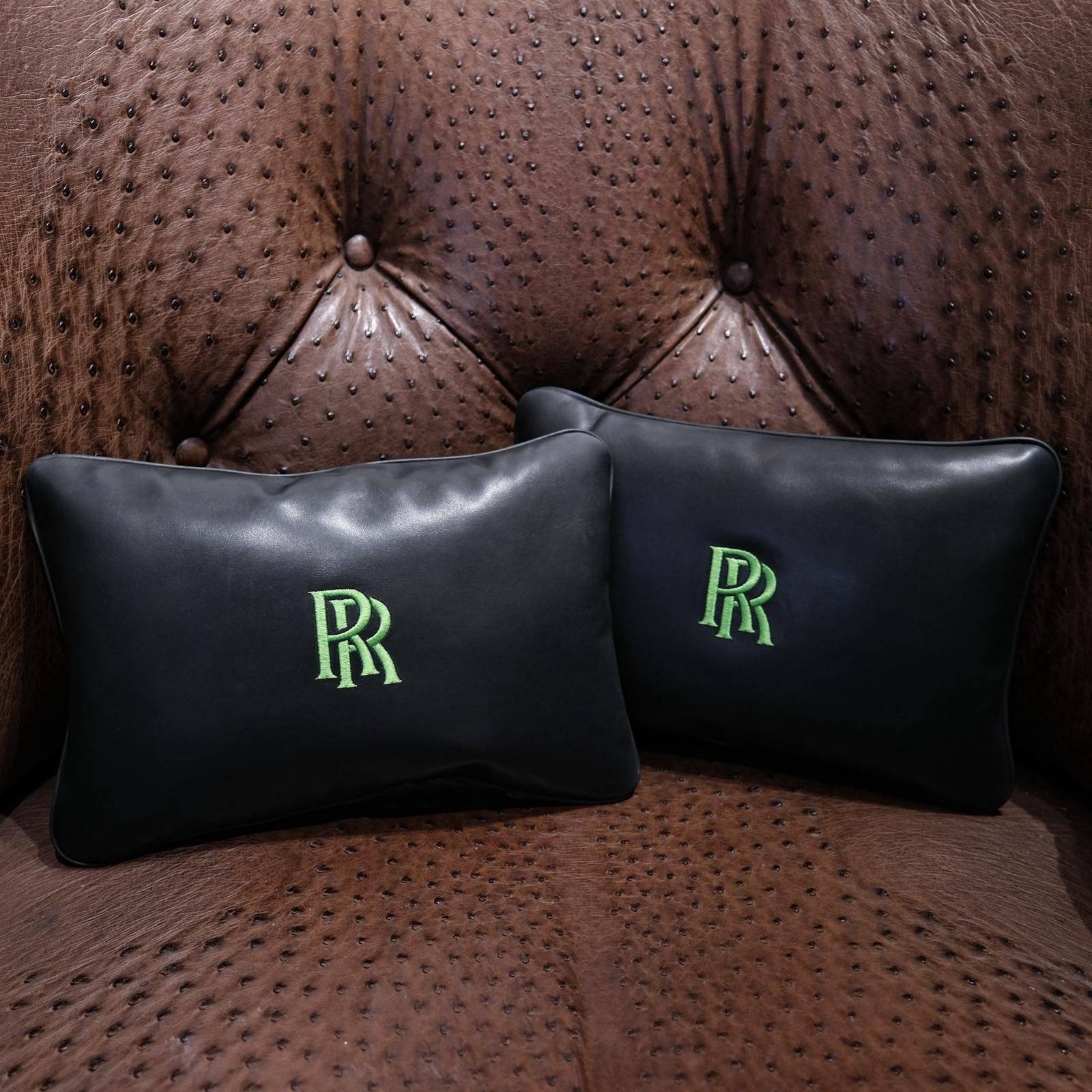 Deux coussins en cuir noir brodés d'un monogramme vert, sur un fauteuil en cuir d'autruche