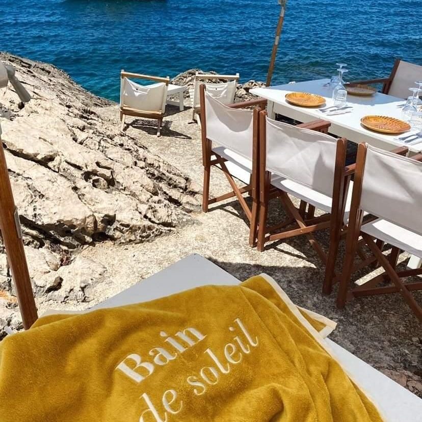 Serviette jaune moutarde brodée « Bain de soleil » devant une table dressée face à la mer